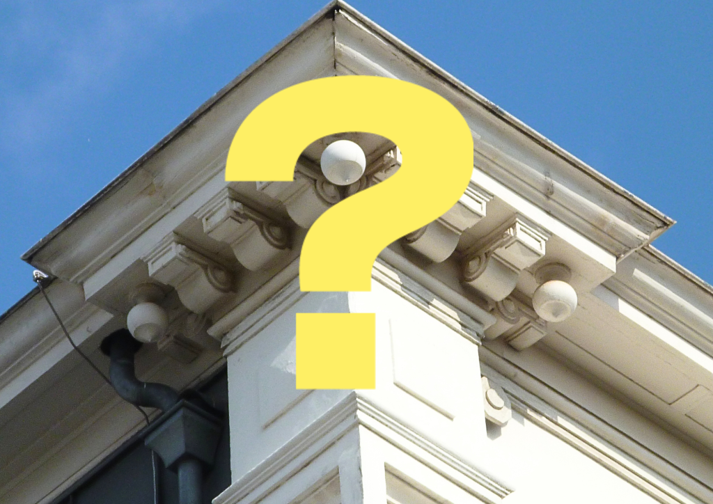 Détail van een kroonlijst in steen van een gebouw met grote vraagteken.